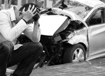 A man beside his crashed car holding his head out of frustration